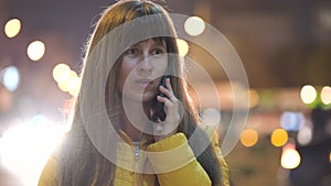 Young pretty woman talking on her mobile phone standing on city street at night outdoors.