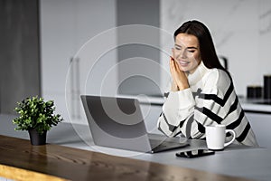 Young pretty woman talking on video call while sitting at table inthe kitchen
