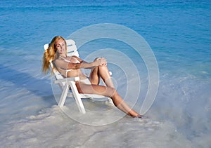 Young pretty woman tans in beach chair in sea