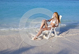 Young pretty woman tans in beach chair in sea