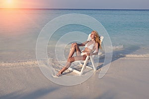 Young pretty woman tans in beach chair in sea , toning