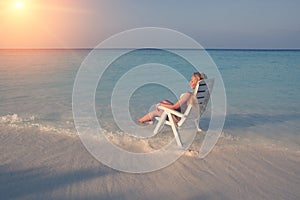 Young pretty woman tans in beach chair in sea , toning