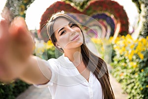 Young pretty woman tourist take selfie on the phone in miracle garden with colorfull frowers hearts