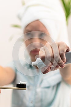 A young pretty woman with a towel on her head in a bright bathroom spreads toothpaste on a toothbrush against the background of a