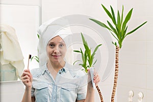 A young pretty woman with a towel on her head in a bright bathroom with a toothbrush and paste in her hands