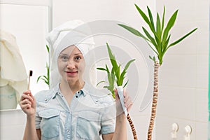 A young pretty woman with a towel on her head in a bright bathroom with a toothbrush and paste in her hands against the background