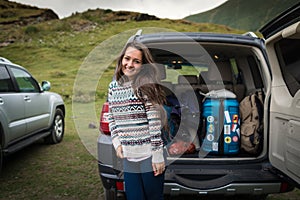 Young pretty woman traveler standing near open back door of the car