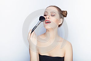 Young pretty woman trendy makeup bright red lips bun hairstyle bare shoulders act the ape with brush white studio background