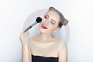 Young pretty woman trendy makeup bright red lips bun hairstyle bare shoulders act the ape with brush white studio background