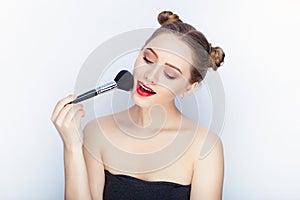 Young pretty woman trendy makeup bright red lips bun hairstyle bare shoulders act the ape with brush white studio background