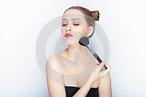 Young pretty woman trendy makeup bright red lips bun hairstyle bare shoulders act the ape with brush white studio background