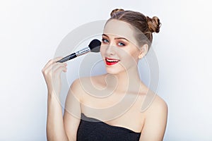Young pretty woman trendy makeup bright red lips bun hairstyle bare shoulders act the ape with brush white studio background