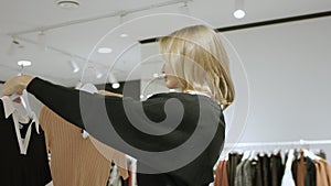 Young pretty woman is trying to pick a blouse at clothing store, tracking shot, 360 degree, close up