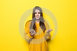 Young pretty woman typing on the phone or serf in internet wearing in yellow sweater isolated on yellow background photo