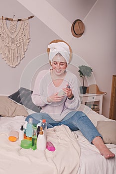 Young pretty woman using care product beauty treatment, skin care. Girl   relaxing on her bed, applying cosmetics, taking care of