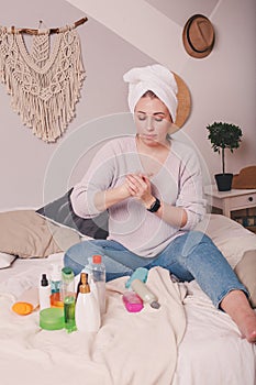 Young pretty woman using care product beauty treatment, skin care. Girl   relaxing on her bed, applying cosmetics, taking care of