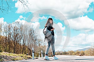 A young pretty woman walks along the countryside road with a backpack in her hands. Back view. Copy space. Concept of