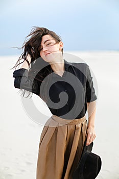 Young pretty woman wearing black blouse and brown skirt standing in white background and keeping hat.