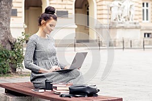 A young pretty woman is working on laptop computer near building of university.