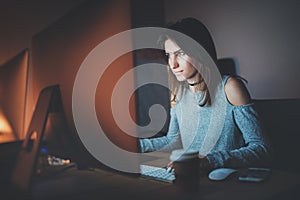 Young pretty woman working on modern studio office at night. Girl using contemporary desktop computer, blurred