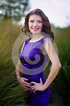 Young pretty women with long windy hair in elegant violet dresses standing on green grass