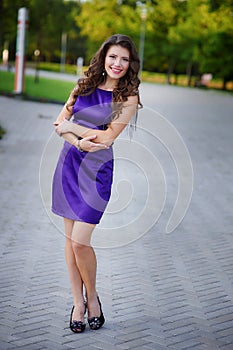 Young pretty women with long windy hair in elegant violet dresses standing on green grass