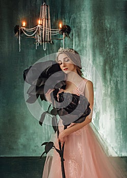 The young princess embraces fabulous, huge, black roses in the Gothic style. The girl has a crown and a luxurious, lush