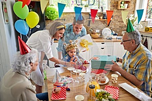 Young princess girl with an inflatable crown on her head, sitting by the table celebrating her birthday with family memebers photo