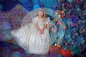 Young princess in a white dress with a tiara on her head at the Christmas tree