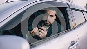 Young private detective man sitting inside car and photographing with dslr camera