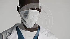 Young professional African American male doctor in medical mask looking serious on camera isolated on white background