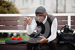 Young professional african american videographer holding professional camera with pro equipment. Afro cameraman wearing black