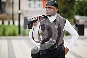 Young professional african american videographer holding professional camera with pro equipment. Afro cameraman wearing black