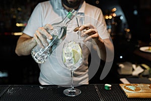 Young professional bartender pours alcohol from a bottle into a glass at a nightclub or bar. Cooking delicious original cocktail