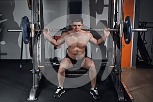 Young professional bodybuilder working out doing squats with barbell.