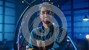 Young Professional Fabricator in Safety Glasses and Apron Gently Smiles at the Camera with Crossed