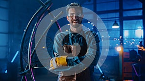 Young Professional Fabricator in Safety Glasses and Apron Gently Smiles at the Camera with Crossed photo