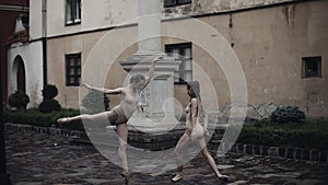 Young professional female dancers is performing acrobatic dance along the medieval street under the rain. Wet girls