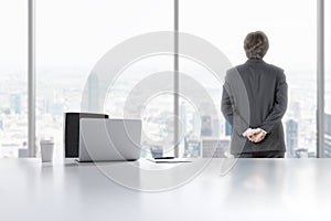 A young professional is looking out the window in the modern panoramic office in Manhattan, New York City. A laptop, notepad and a