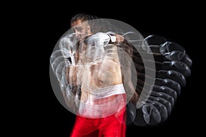 Young professional male boxer in red shorts and boxing gloves training, exercising over black studio background.