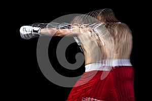 Young professional male boxer in red shorts training, exercising over black background. Stroboscope