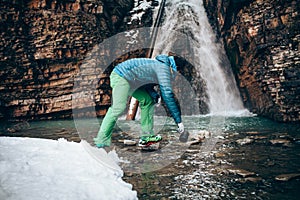 Young professional male tourist collects water from a mountain river.in winter.