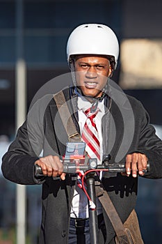 Young professional man wearing a business suit, helmet and a tie on a scooter, enjoying a ride