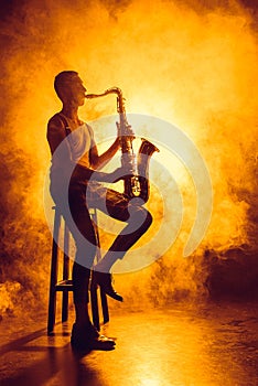 young professional musician sitting on stool and playing saxophone