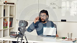 Young professional programming tutor recording video tutorial for his blog on professional digital equipment. Looking at photo
