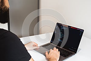 Young professional software engineer, IT specialist, programmer, working at home and writing code on a laptop computer.