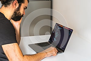 Young professional software engineer, IT specialist, programmer, working at home and writing code on a laptop computer.