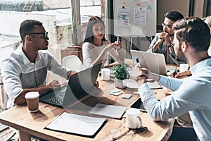 Young professional team. Top view of young modern people in smart casual wear discussing business while working in the creative o photo