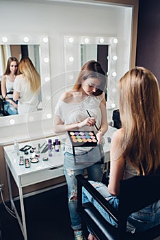 Young professional visagiste holding palette applying eyeshadow to the Caucasian female model in beauty shop