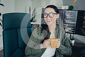 Young professional woman programmer working remotely on coding tasks in a modern office workspace holding coffee